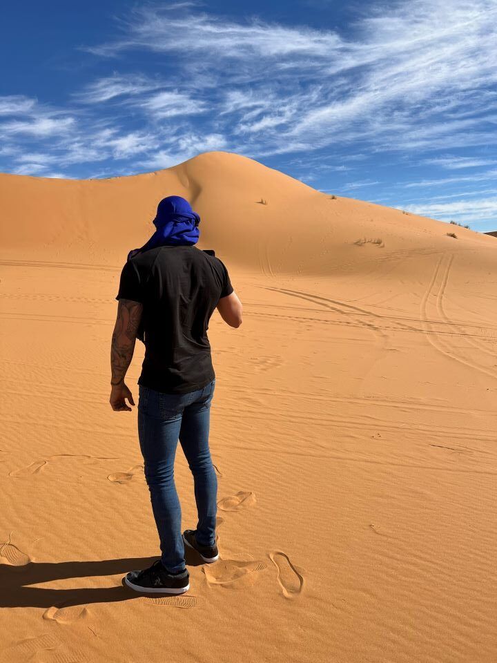 chica haciendo una foto con el movil de espaldas con trapo en la cabeza azul en la dunas del desierto en marruecos